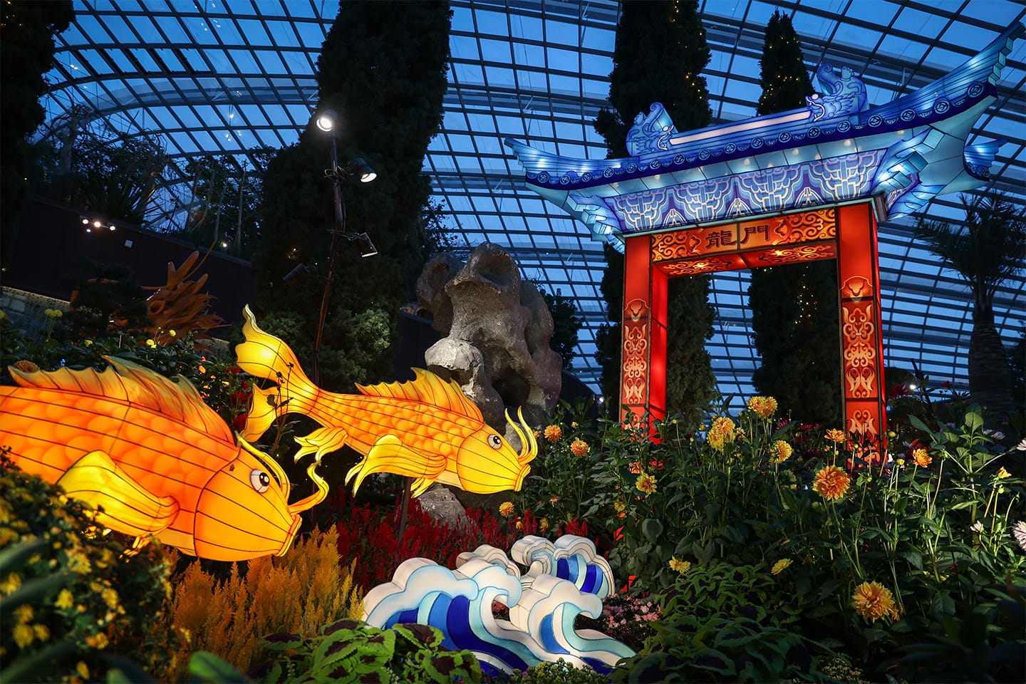 Illuminated koi and wave decorations beneath glass roof, near red and blue Chinese gate.